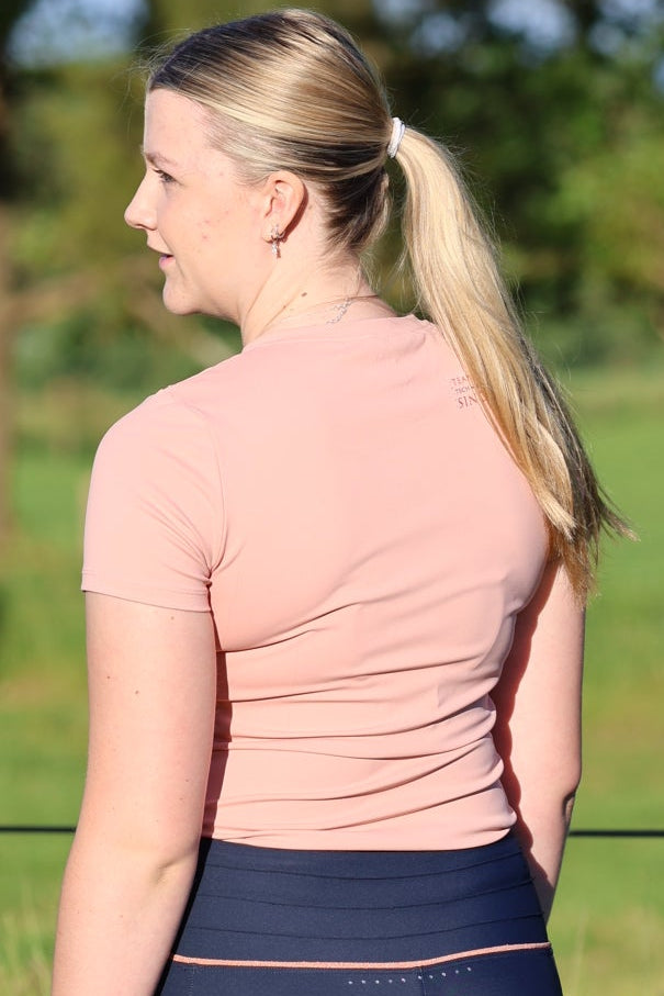Person wearing a pink top and blue leggings standing on grass with trees in the background