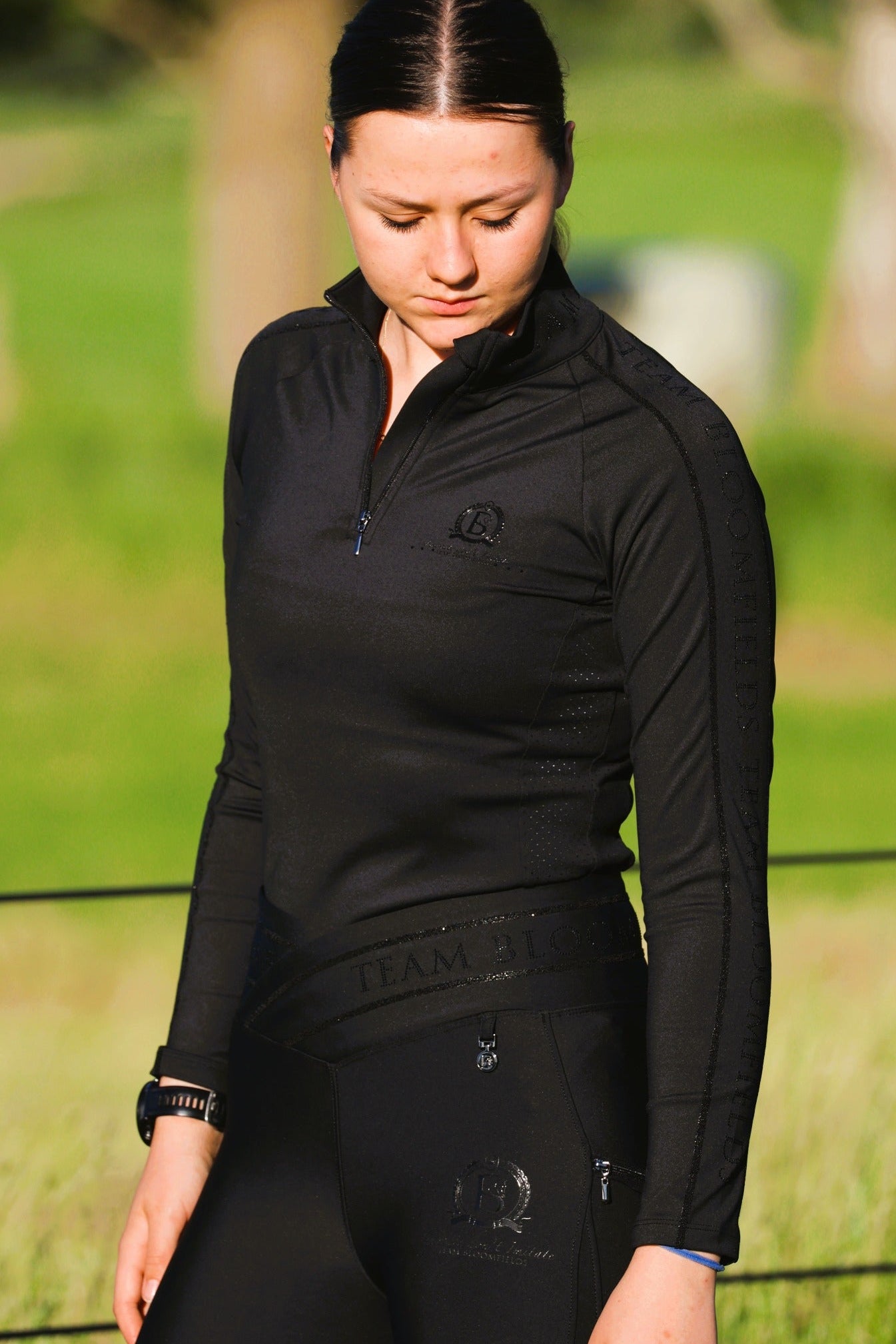 Person wearing a black riding outfit with a logo in an outdoor setting