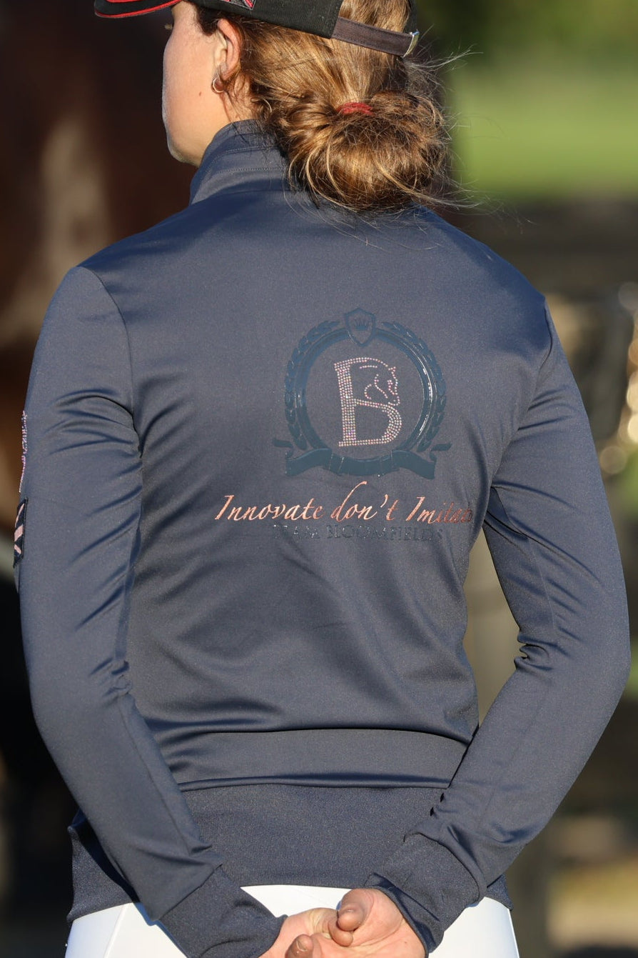 Person wearing a navy blue jacket with a logo, standing next to horses in an outdoor setting.